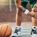 A man playing basketball holds his knee in pain