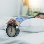 A woman turns off her alarm clock to go back to sleep